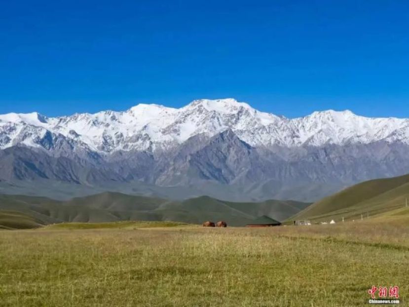 层云叠雪峰，层叠流云横向铺开在昆仑雪峰上空，蓝天做底色，云朵错落有致，雪山纹理清晰。