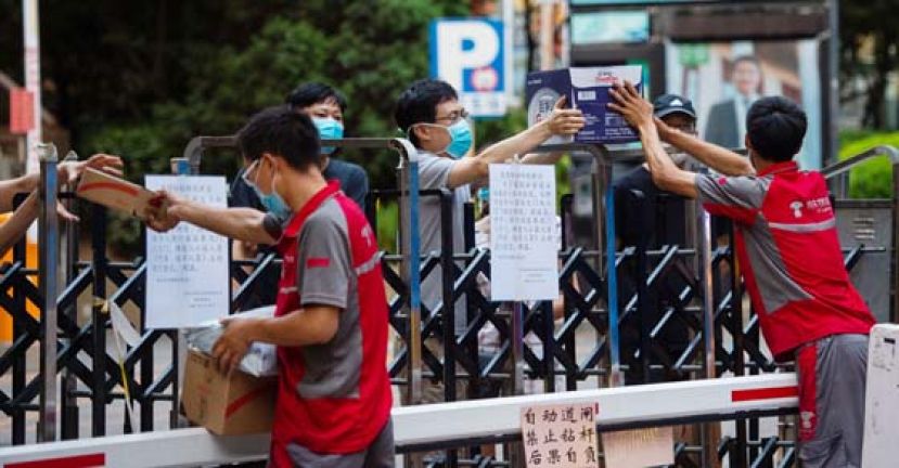 快递员在围栏外为居住在北京市西城区广外街道手帕口南街社区的居民递送包裹。