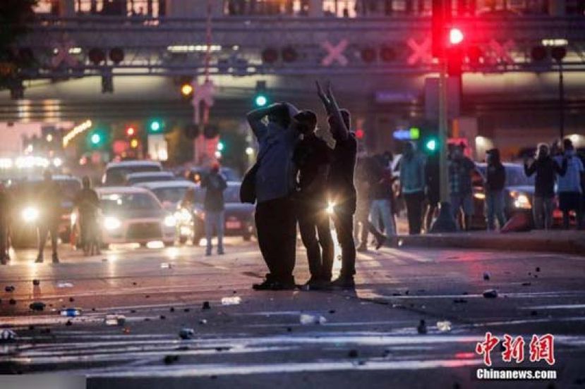 当地时间5月28日，美国明尼苏达州明尼阿波利斯市抗议示威活动继续进行，示威者举起双手站在马路上的碎片中。