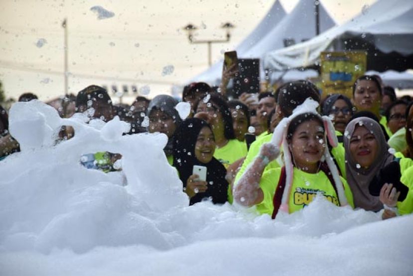 “泡沫”慈善义跑参与者童心未泯的玩起堆积在起跑点的泡沫。