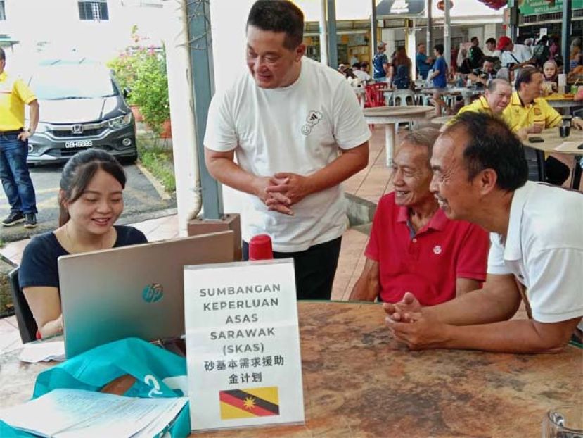 巴都林当区议员施志豪（站者）与其助理曼丽（左）积极协助各族民众跟进砂政府福利的申请程序。