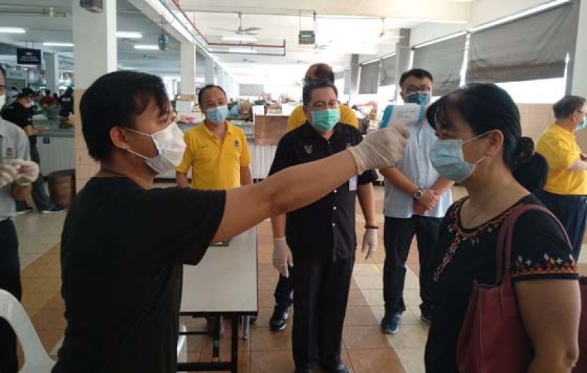 工作人员在实都东菜市场为顾客测量体温。中为南市市长拿督黄鸿圣。