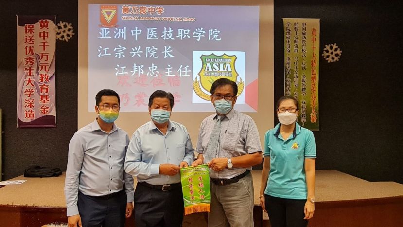 砂医总会长兼亚洲中医技职学院院长江宗兴（左2）联袂主任江邦忠（左1）赠送锦旗予黄乃裳中学校长卢友雄；右1为王铃雁老师。
