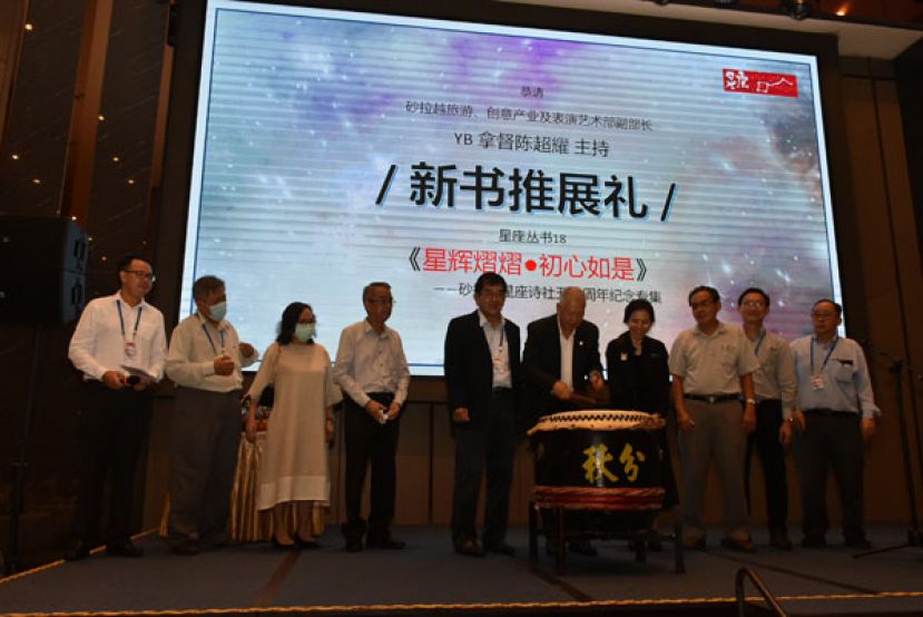 砂拉越旅游、创意工业和表演艺术部副部长拿督陈超耀（中）击鼓推展50周年纪念专集。