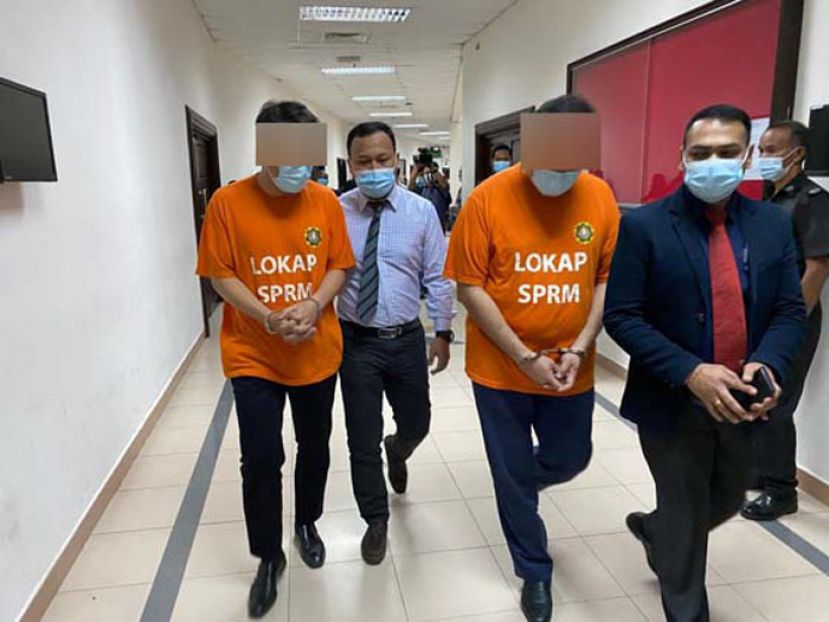 2名拿督级嫌犯带着手铐，由反贪污会官员押上法庭。
