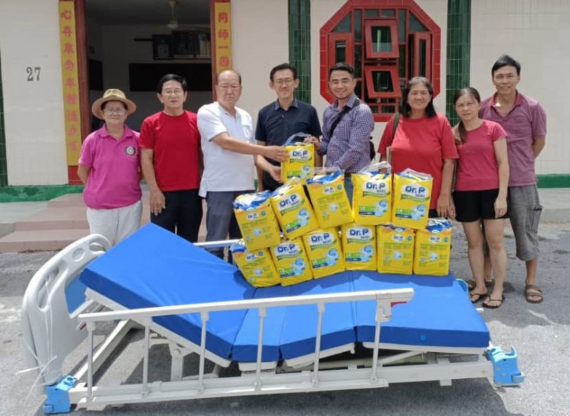 砂同心善堂主席黄国远（左3）移交护理床及纸尿裤用品予长期卧病在床男子亲属；左4为见证人薛华东及该善堂理事等人。