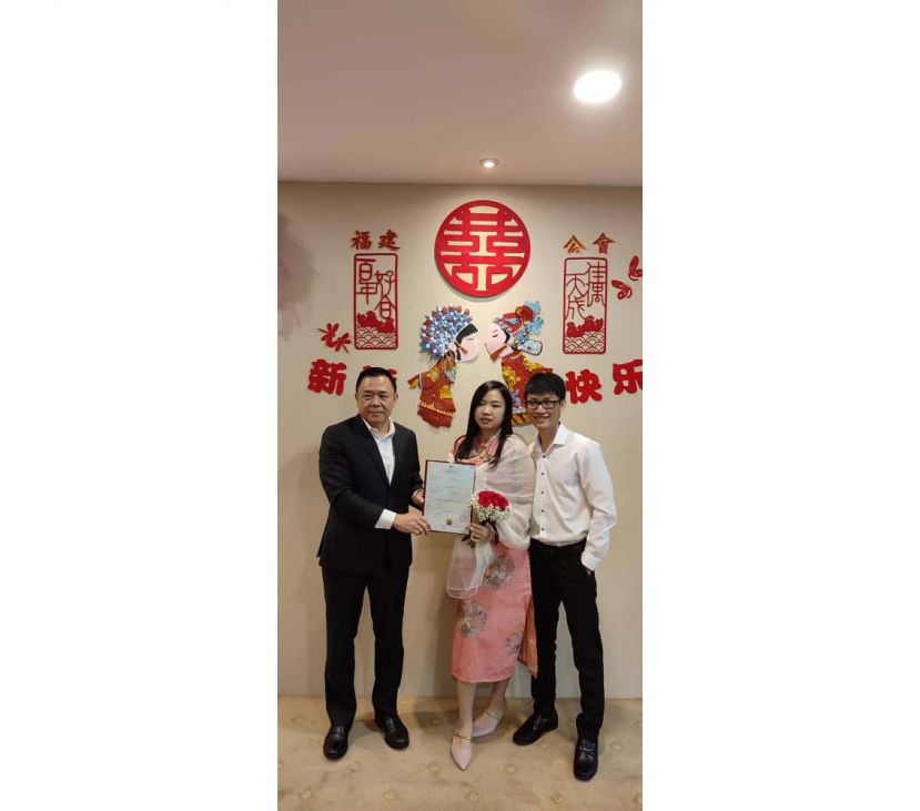 一对新人刘春杰和戴杏艾从福建公会婚姻注册官刘金瑞（左）手中接过结婚证书时摄。