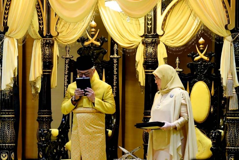 图：苏丹阿都拉在宣誓就任彭亨第六任苏丹的仪式上亲吻可兰经。右为苏丹后东姑阿兹莎。