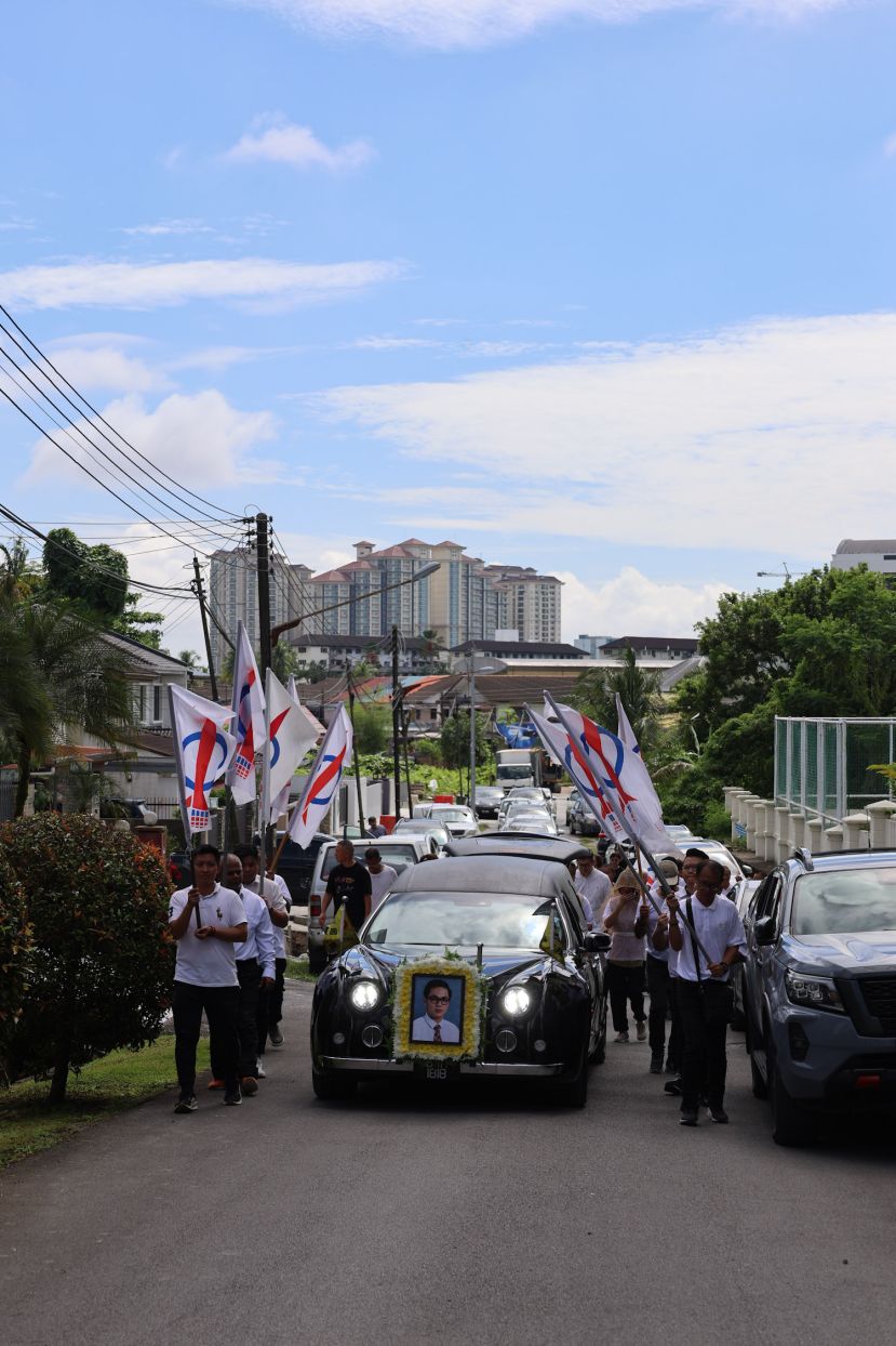 行动党党员手持火箭旗帜，护送灵车缓步驶出治丧处。